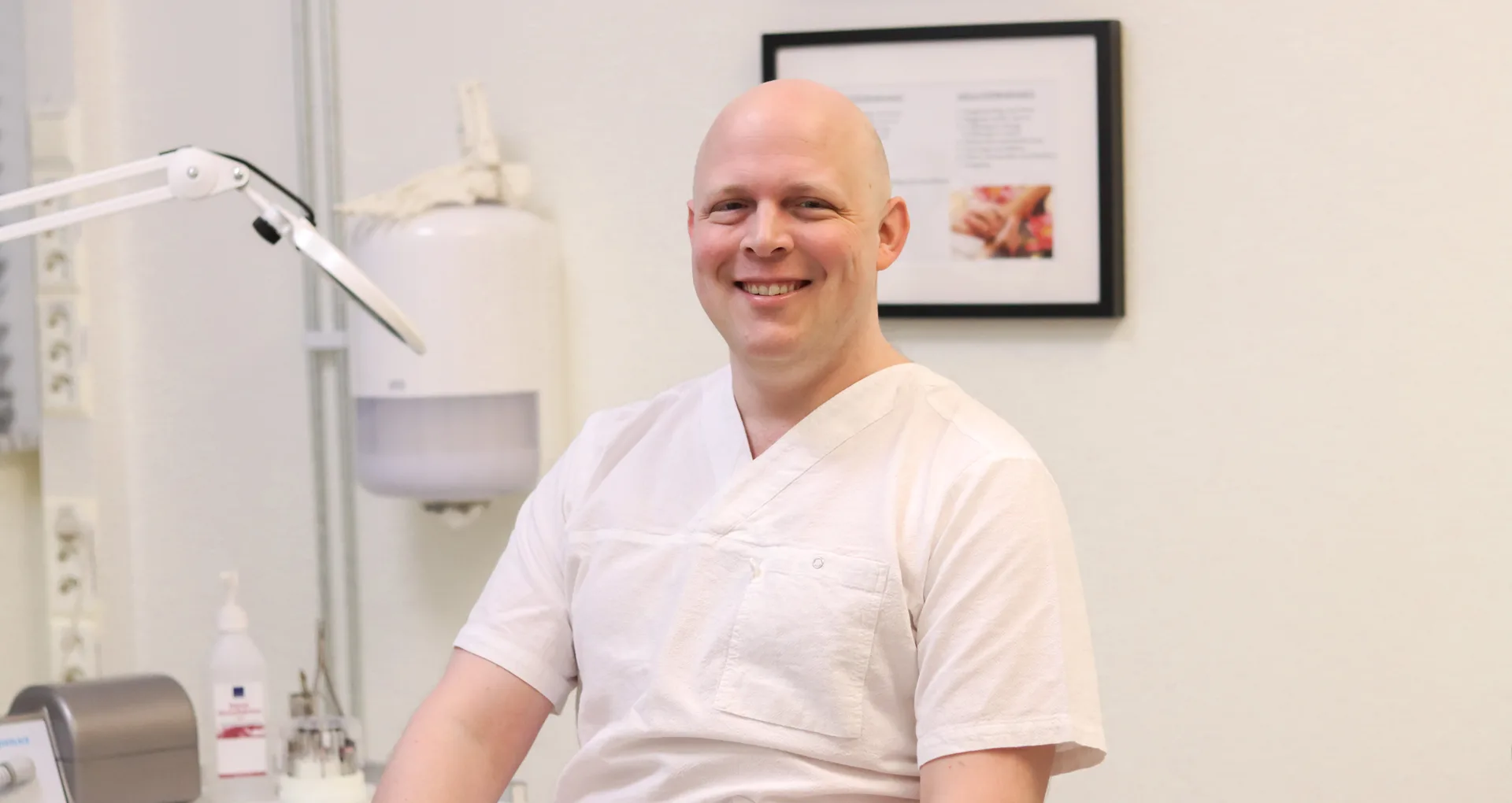 Leende manlig medicinsk fotterapeut som sitter i ett behandlingsrum.