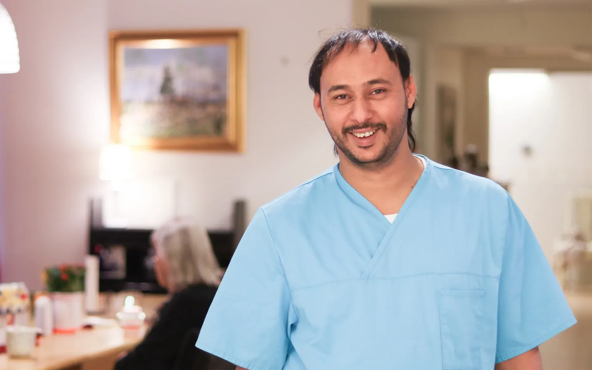 En manlig undersköterska på ett äldreboende som ler in i kameran.