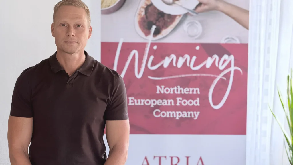 Ulrik Jismyr som är med i ledningsgruppen för Processtekniker inom hållbar livsmedelsproduktion står vid en skylt där det står Winning Northern European Food Company Atria. Han har blont kort hår och bär en brun pikétröja