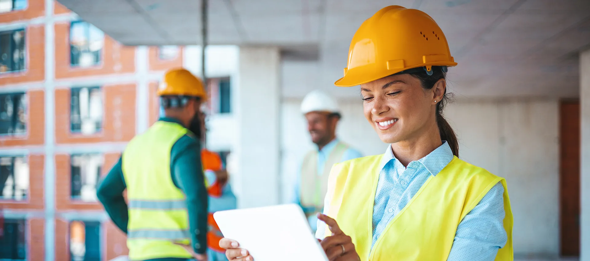 En kvinna i skyddshjälm och väst håller i en padda. I bakgrunden syns tre personer, också de i hjälm och väst.