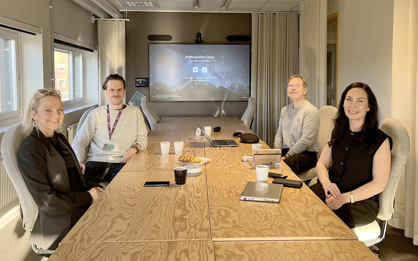 Vid ett skrivbord i ett konferensrum sitter fyra personer. På vänster sida om bordet sitter Katarina Tinderdahl och Gustav Hedenborg och mitt emot sitter två representanter för Skelllefteå Kommun. I bakgrunden syns en stor bildskärm.