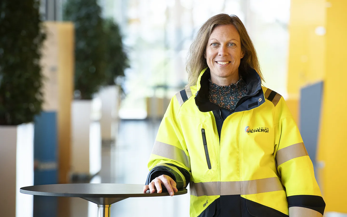Hanna Tengliden, driftchef på Jönköping Energi står i en gul varseljacka i ett kontorslandskap. Hon lutar sig mot ett ståbord och ler in mot kameran.