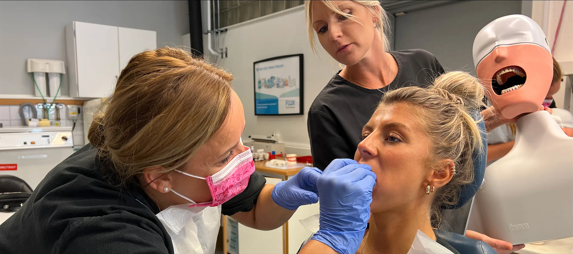 Två kvinnliga studerande arbetar i dentalrummet under handledning av föreläsare.