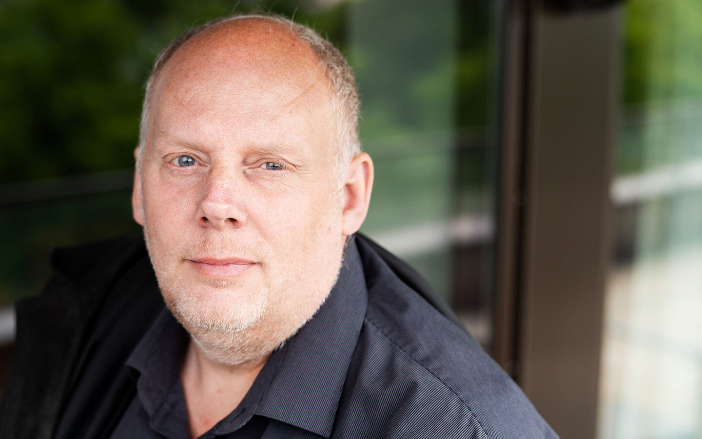 Porträttbild på Matts Spångberg där Matts syns i vänstra delen på bild i lätt fågelperspektiv. Matts har en svart skjorta och i bakgrunden syns ett fönsterparti. 