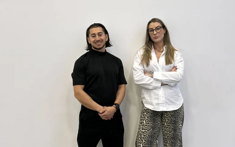 Johannes Ojanperä och Amanda Sörensen poserar framför en vit vägg. Johannes har mörkt axellångt hår och klädd helt i svart. Amanda har långt, brunt hår, bär mörka glasögon och en vit skjorta med mörka byxor.