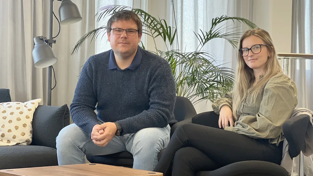 Kristoffer och Felicia sitter i varsin fåtölj och tittar in i kameran. Kristoffer har kort, brunt hår och glasögon. Han bär ljusa jeans och en mörkblå tröja. Felicia har långt mörkblont hår och glasögon. Hon bär en grön tunika och svarta byxor.