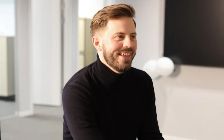 Jacob Linusson sitter i ett öppet kontorslandskap. Han har kort, brunt hår och kortklippt skägg. Han bär en svart polotröja. Jacob ler och tittar åt höger.