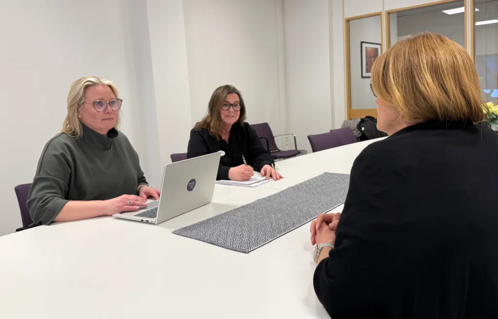 Jenny Jakobsson och Kristin Grude sitter vid ett konferensbord och för ett samtal med en kvinna som sitter mitt emot dem med ryggen mot kameran.