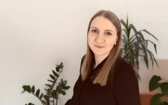 Johanna Fasth som tagit emot en LIA-studerande tittar in i kameran och ler. I bakgrunden syns ett kontorslandskap med gröna växter.