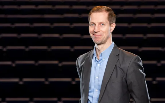Stefan Englebrektsson som berättar hur utbildning ger självförtroende står till höger i bilden och tittar in i kameran. Bakgrunden är mörk med suddiga ränder.