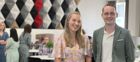 Michelle och Tage står festklädda i TUCs examensprydda lokaler. De ler in mot kameran.